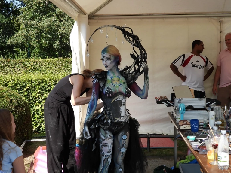 Künstler arbeitet im Festivalzelt an einem silbern bemalten Model mit großem Kopfschmuck