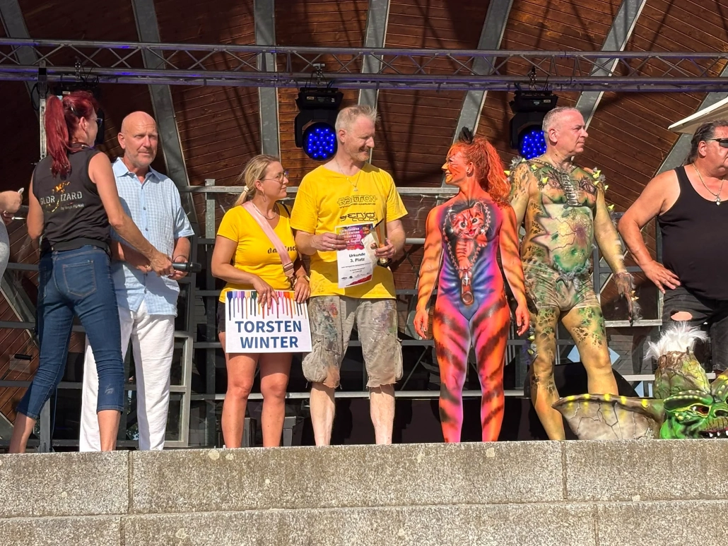 Bodypainting-Models, Organisatoren und weitere Beteiligte stehen in einer Reihe auf der Festivalbühne