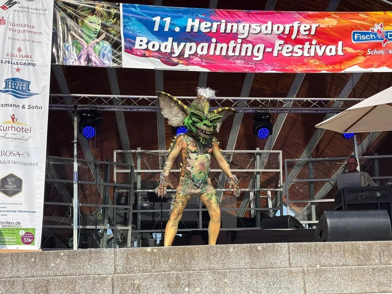 Naturfarben bemaltes Model mit großem Kopfschmuck steht mittig auf der Festivalbühne