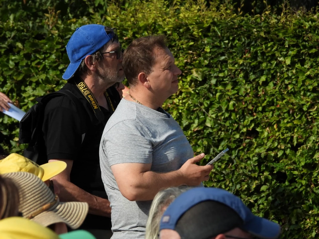 Mehrere Besucher beobachten das Geschehen bei sonnigem Wetter am Rand des Festivalplatzes