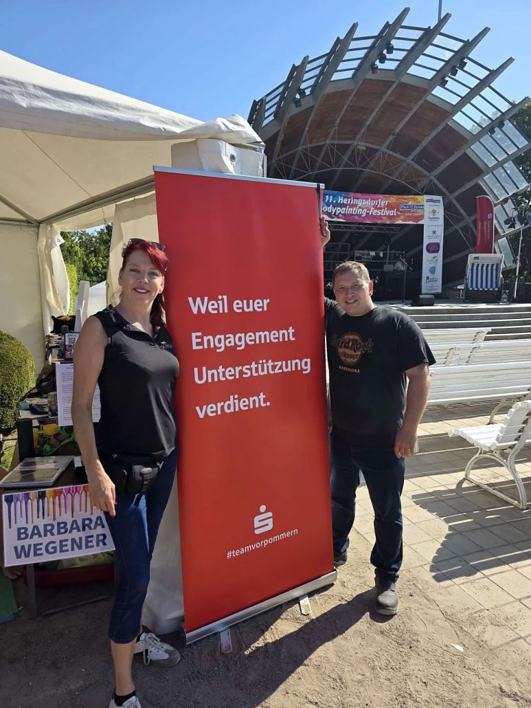 Zwei Personen stehen an einem Informationsstand auf dem sonnigen Festivalgelände