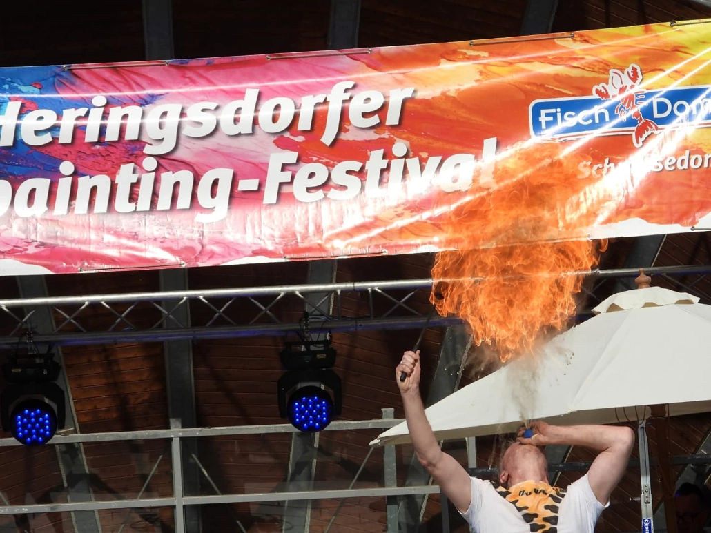 Eine große Flamme steigt während einer Feuershow vor dem Festivalbanner auf
