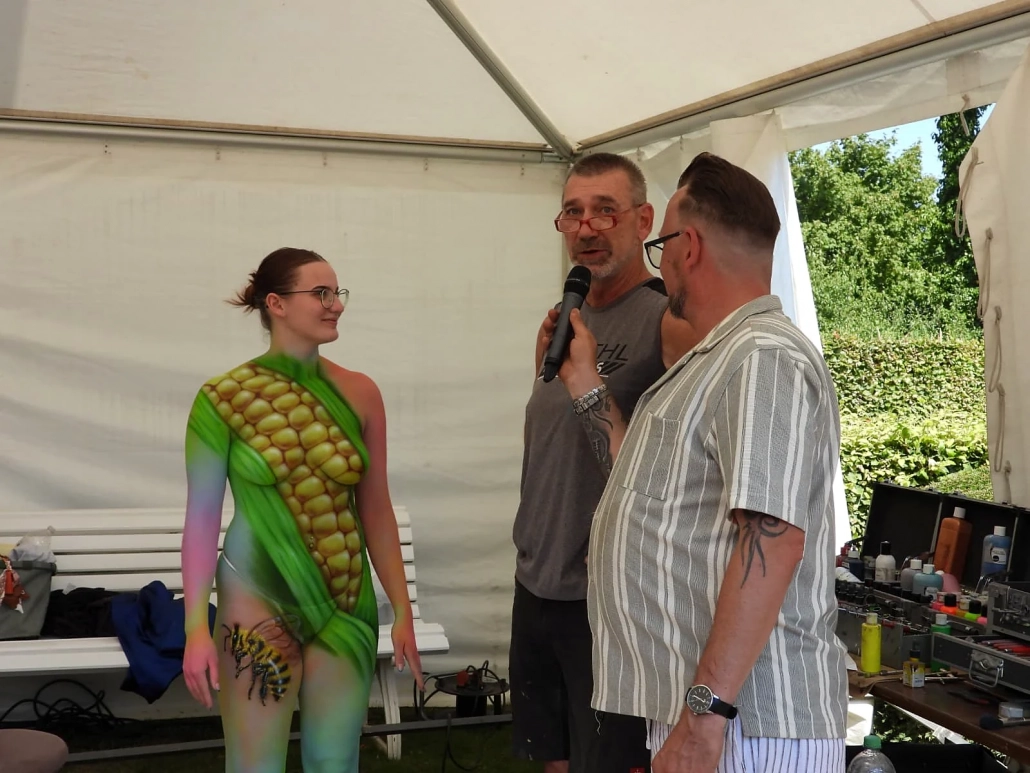 Ein grün bemaltes Model spricht im Festivalzelt mit zwei Männern