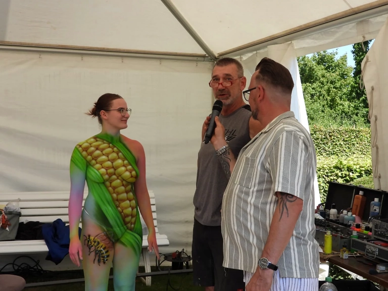 Ein grün bemaltes Model spricht im Festivalzelt mit zwei Männern