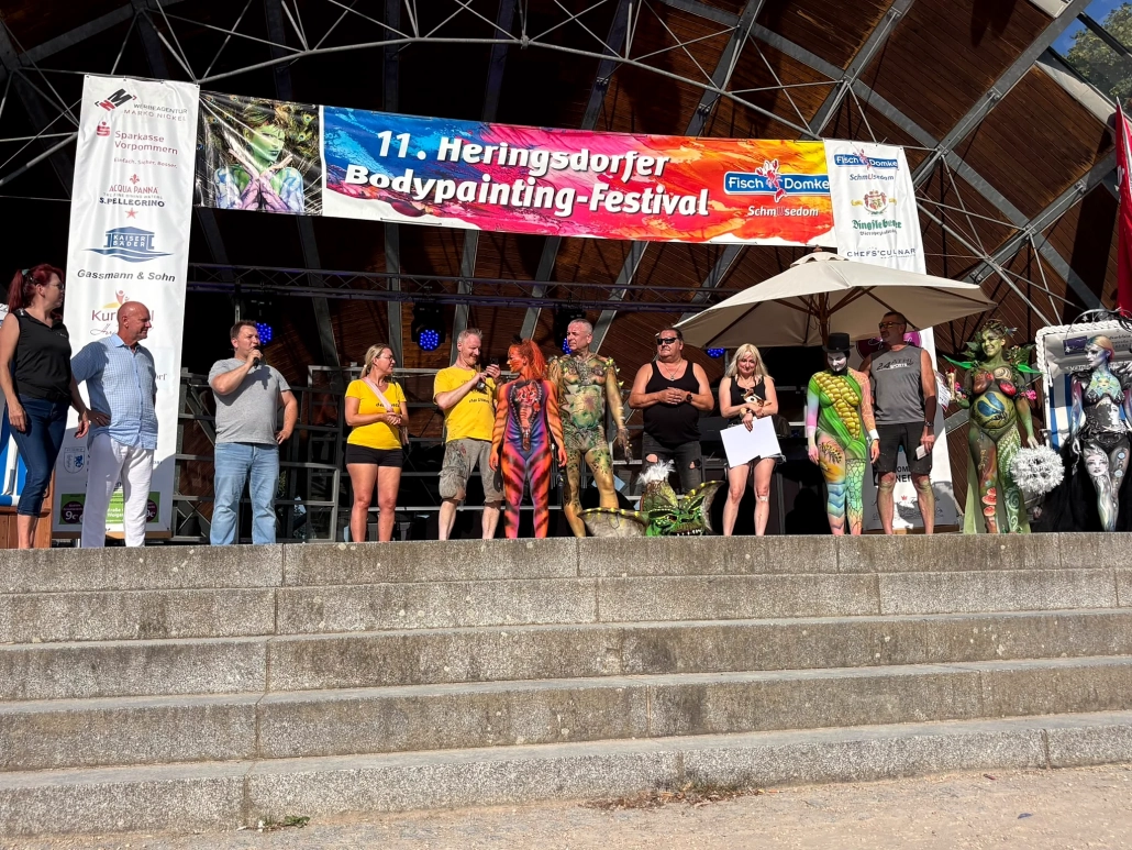 Eine große Gruppe aus Models und Beteiligten steht auf der Bühne über den breiten Treppenstufen
