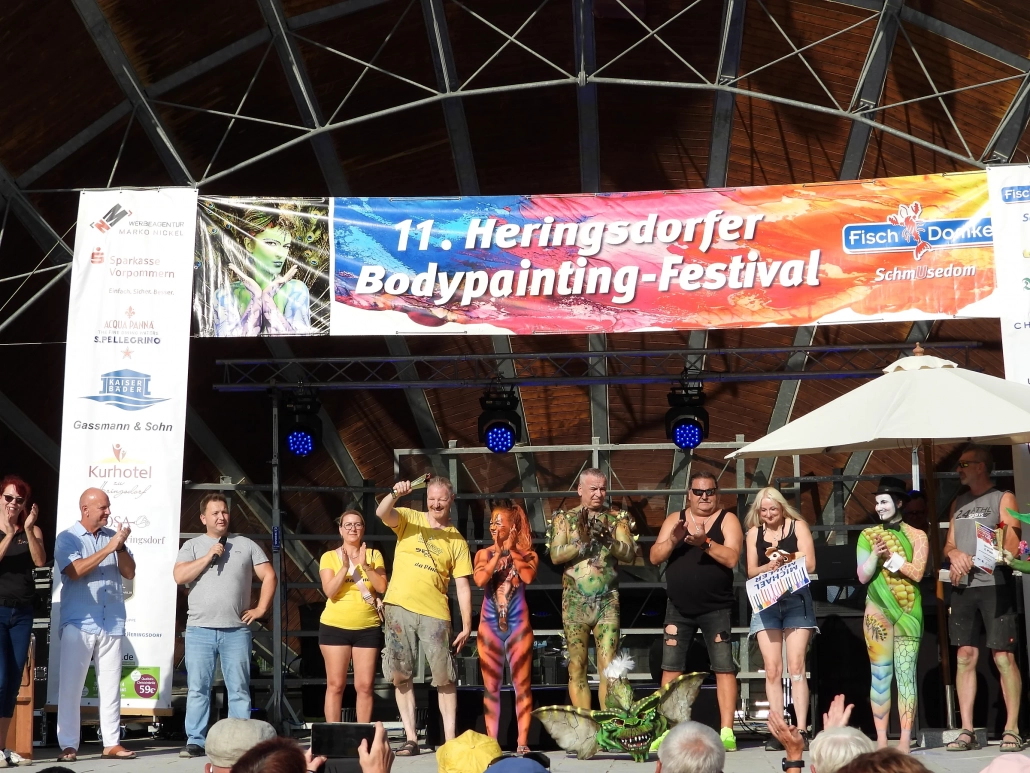 Viele Models, Künstler und Beteiligte stehen gemeinsam vor dem Festivalbanner auf der Bühne
