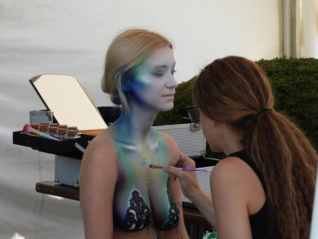 Künstlerin trägt Farbe auf den Oberkörper eines blau-grün bemalten Models auf