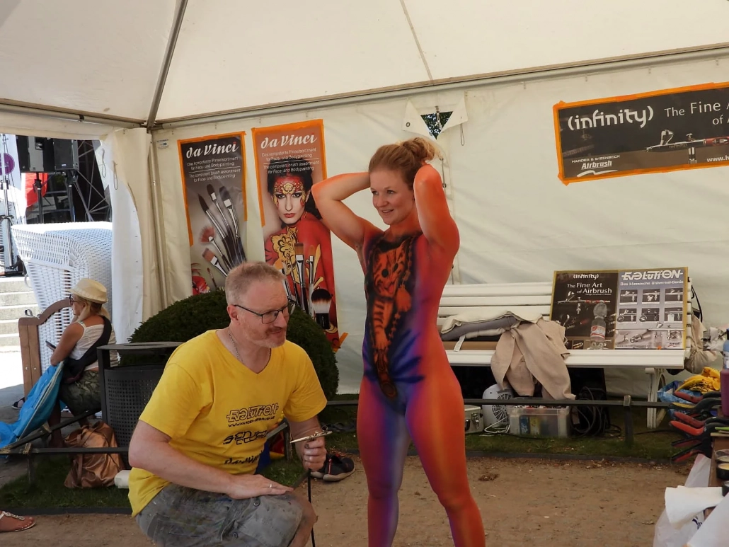 Künstlerin arbeitet im Festivalzelt an einem orange bemalten Model