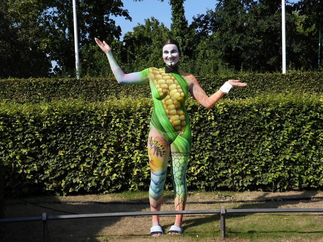 Grün bemaltes Model mit Maiskolben-Motiv posiert im Freien vor einer Hecke