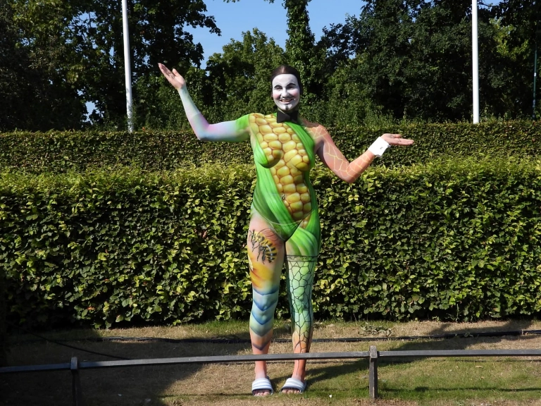 Grün bemaltes Model mit Maiskolben-Motiv posiert im Freien vor einer Hecke