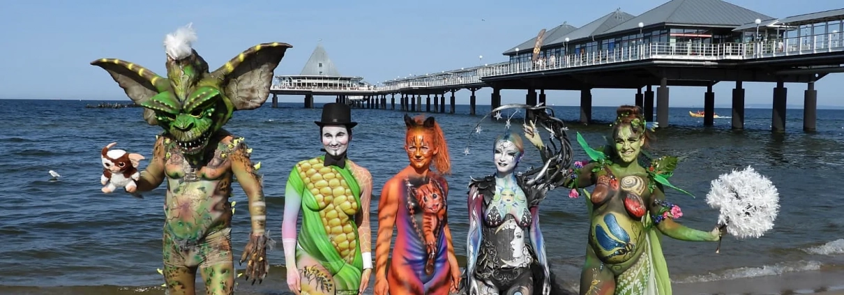 Mehrere fantasievoll bemalte Models stehen am Strand vor der Heringsdorfer Seebrücke