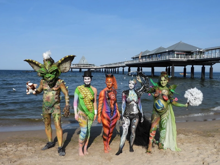 Mehrere fantasievoll bemalte Models stehen am Strand vor der Heringsdorfer Seebrücke