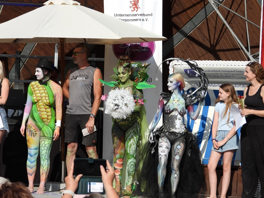 Mehrere Bodypainting-Models und Beteiligte stehen gemeinsam im offenen Festivalzelt