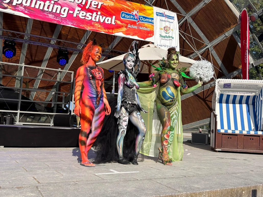 Drei unterschiedlich bemalte Models posieren gemeinsam vor dem Festivalbanner