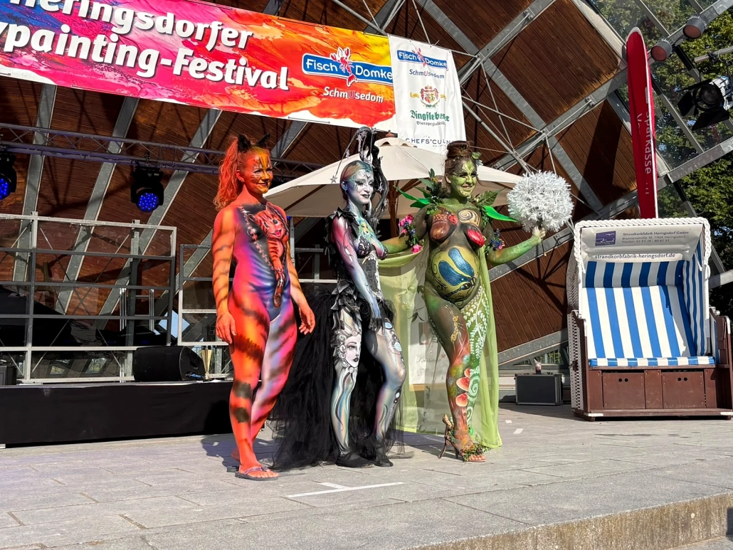 Drei unterschiedlich bemalte Models präsentieren sich gemeinsam auf der Festivalbühne