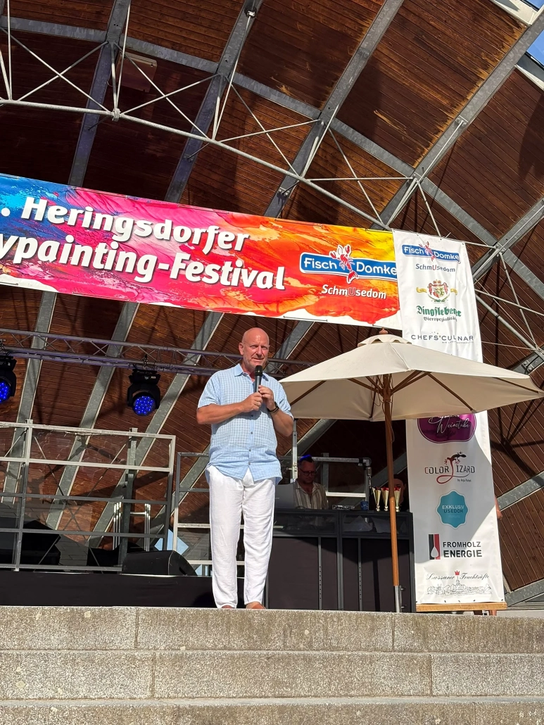 Moderator in heller Kleidung spricht allein unter dem Festivalbanner auf der Bühne