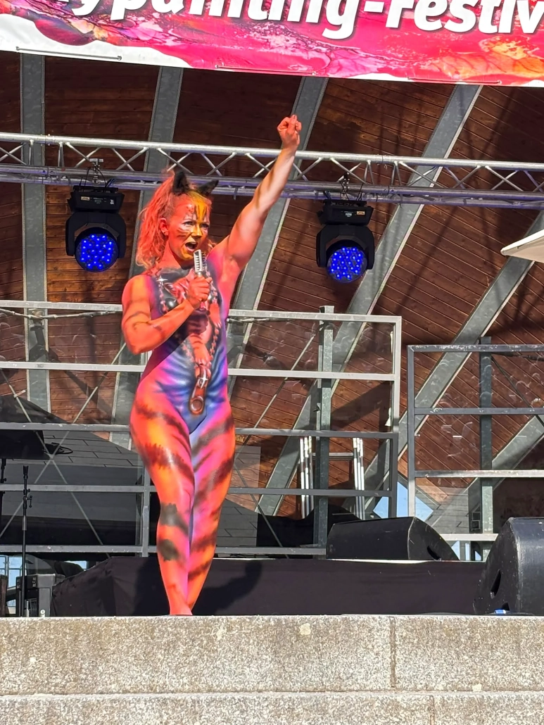 Orange-violett bemaltes Model hebt bei der Bühnenpräsentation einen Arm