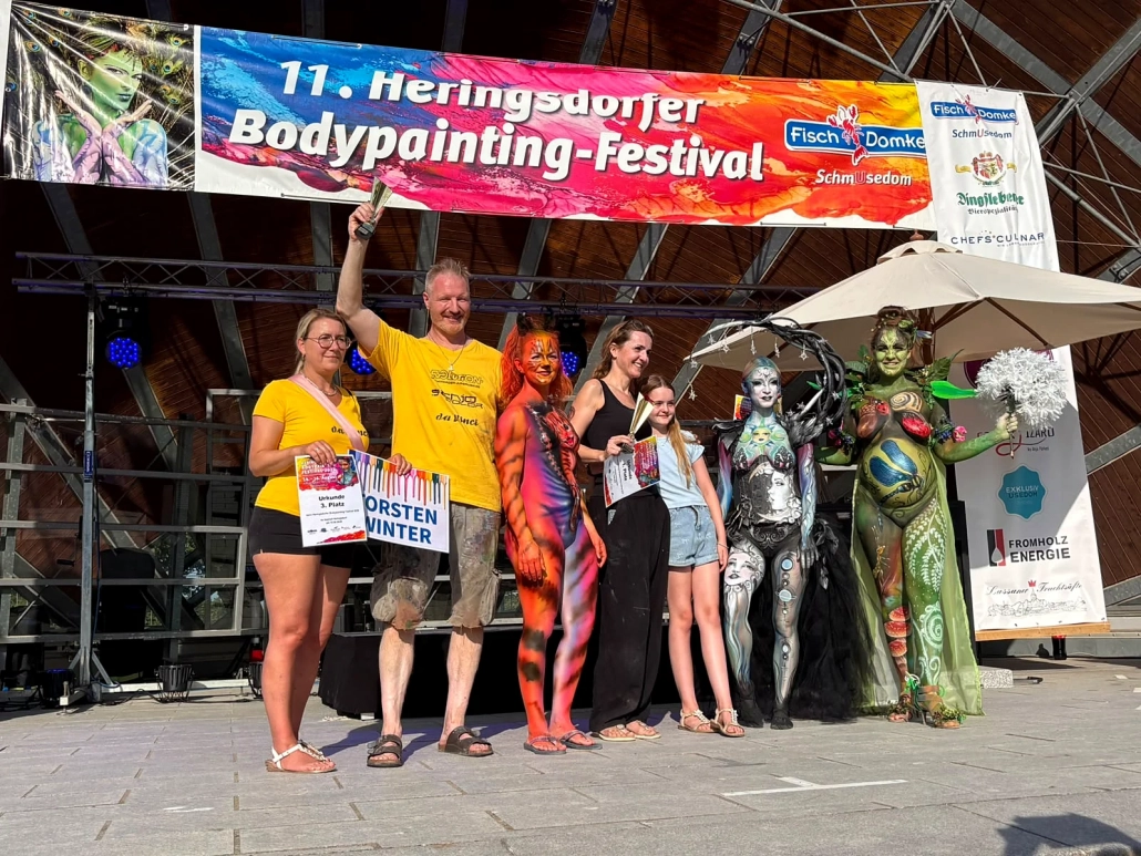Ausgezeichnete Teilnehmende mit Schildern posieren zusammen mit mehreren Bodypainting-Models
