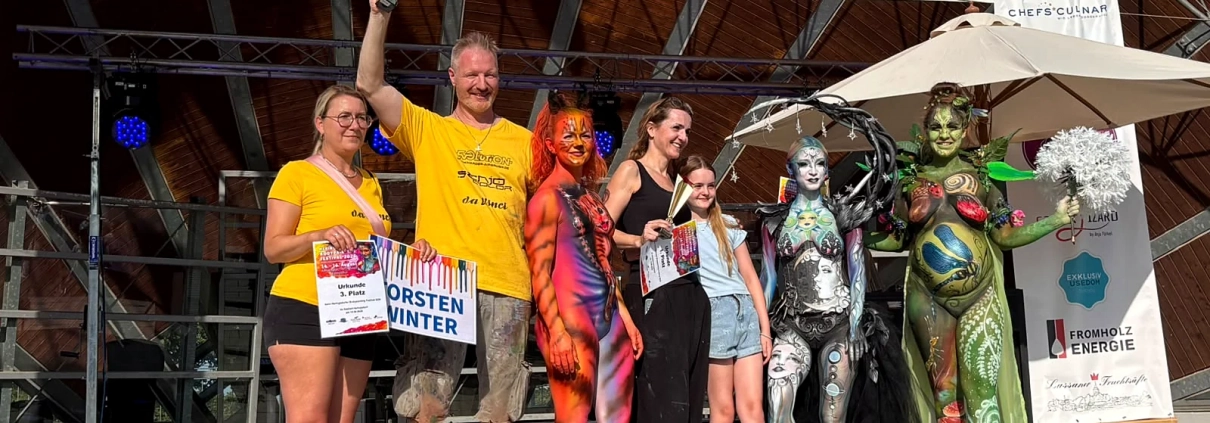 Ausgezeichnete Teilnehmende mit Schildern posieren zusammen mit mehreren Bodypainting-Models