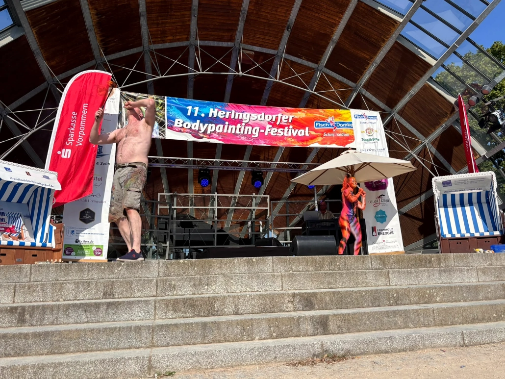 Ein Performer steht während des Rahmenprogramms vor dem Festivalbanner auf der Bühne