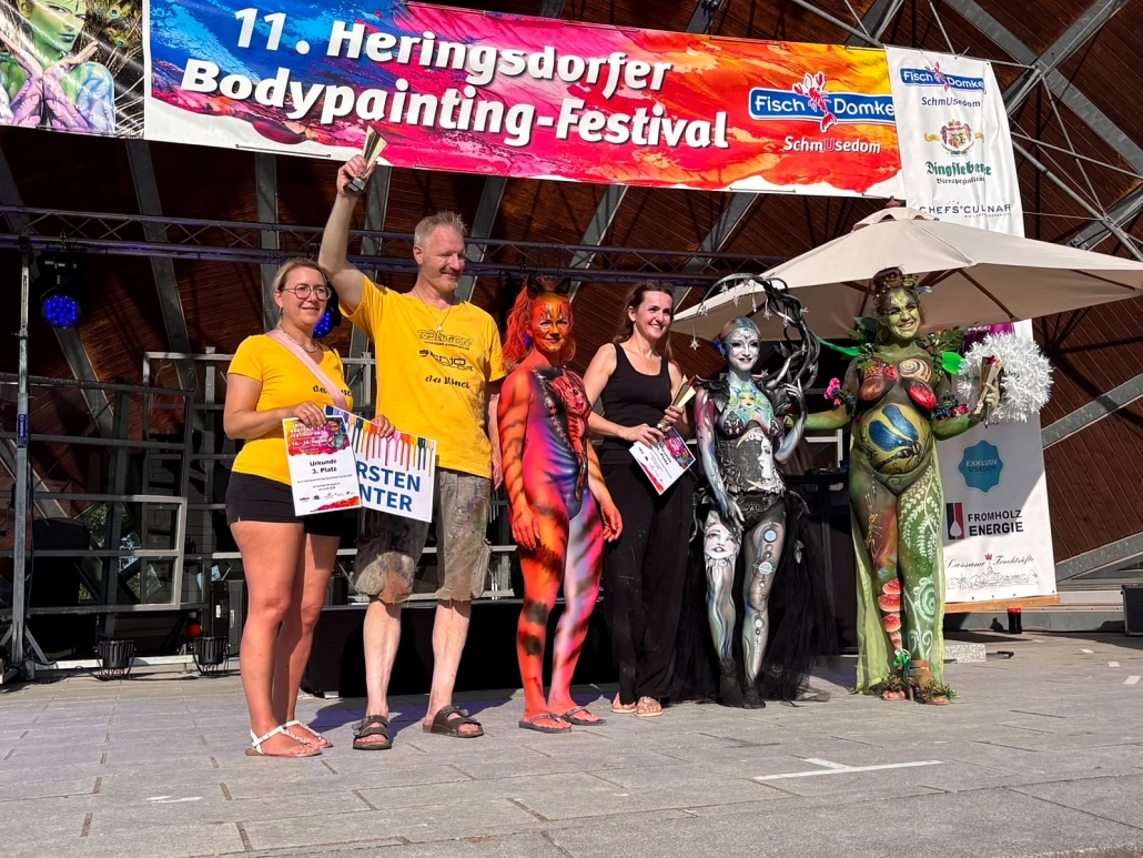 Mehrere ausgezeichnete Teilnehmende und Models stehen gemeinsam vor dem Festivalbanner