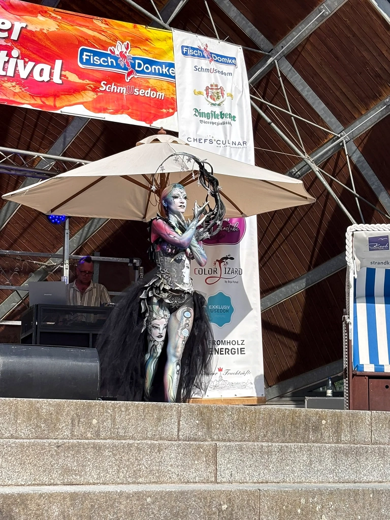 Schwarz-silbern bemaltes Model präsentiert eine ausdrucksstarke Pose auf der Festivalbühne